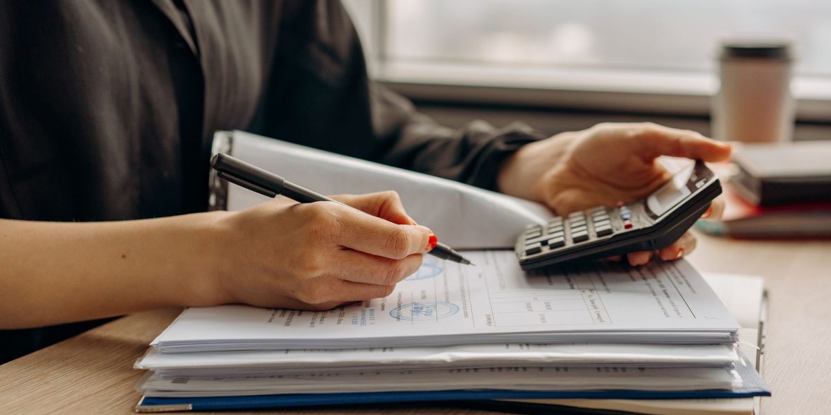 Persoană analizând documente financiare cu un calculator