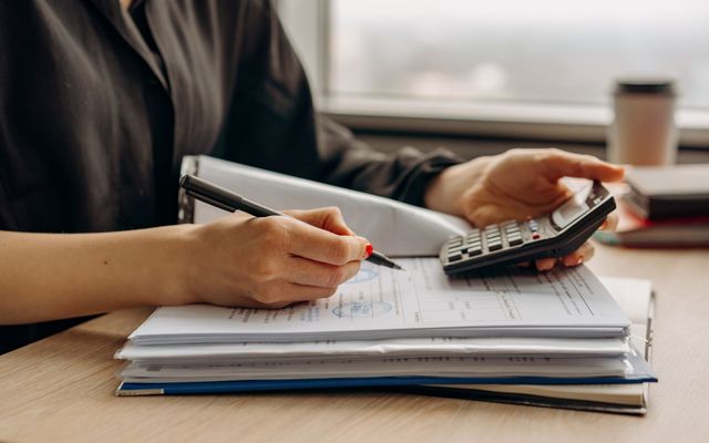 Persoană analizând documente financiare cu un calculator